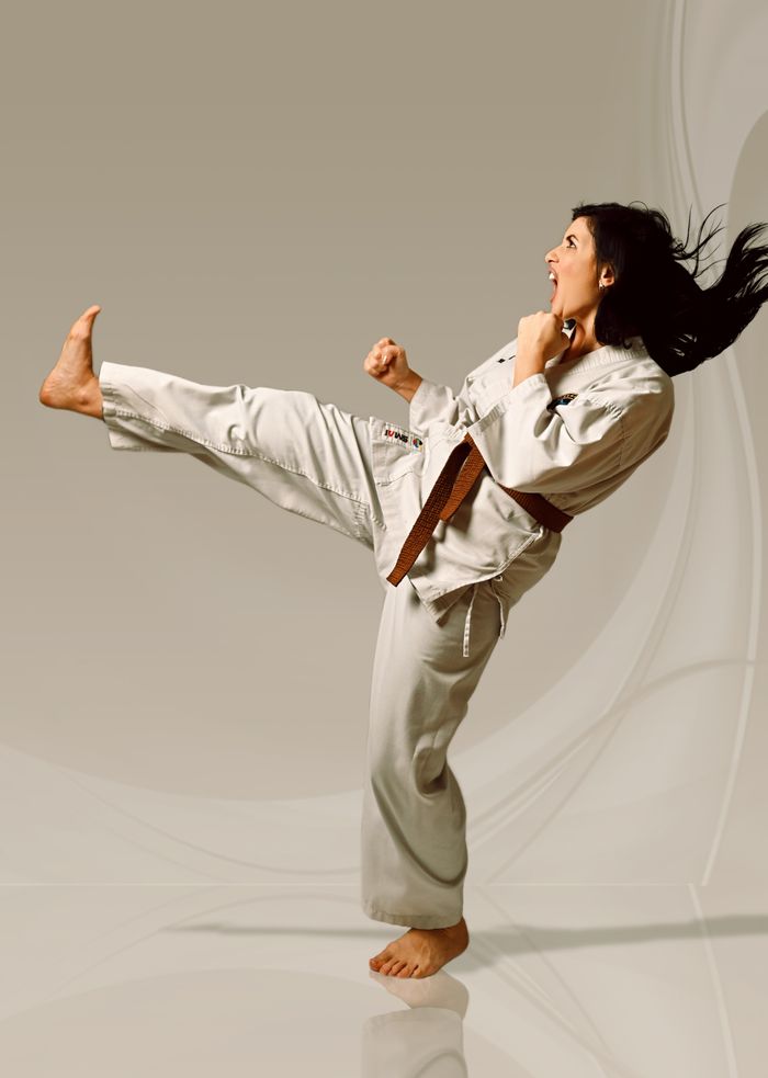 who-we-are Woman in karate gear executing a high kick in studio. Perfect for sports and fitness themes.