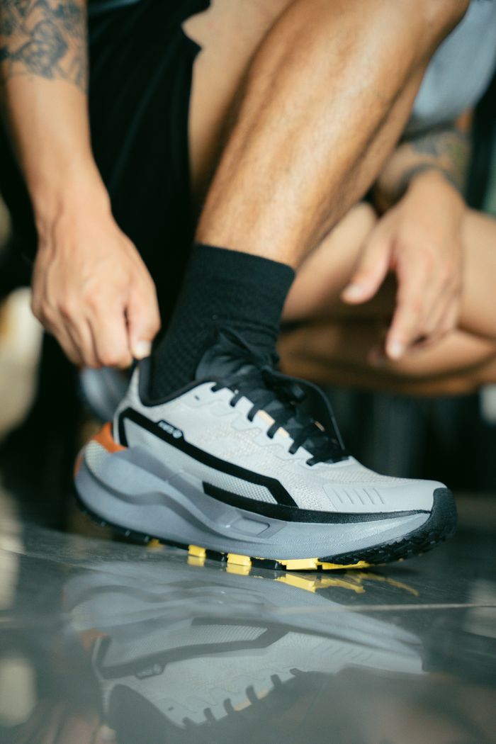 Close-up of a man tying a modern athletic shoe on a reflective surface indoors.