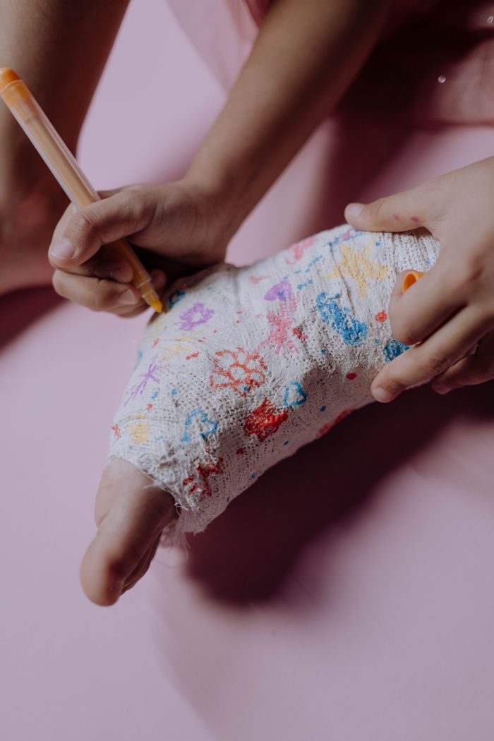 A child's hands drawing on an orthopedic cast with colored pens on a pink background.
