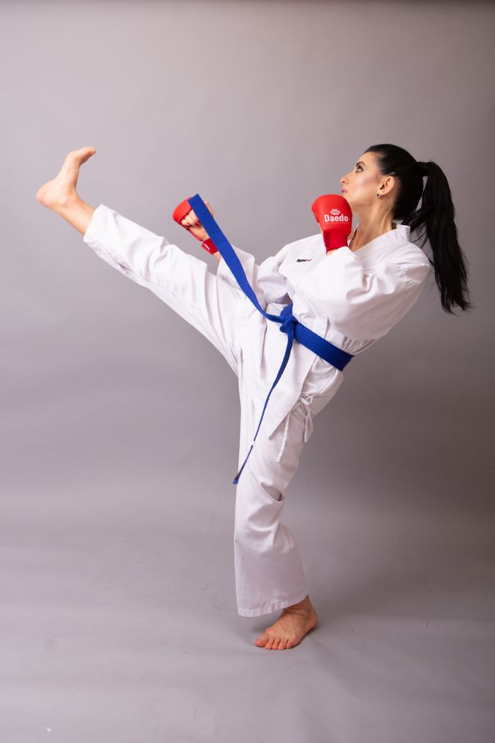 about-bg Side view of professional female athlete in white sportswear and gloves showing kick with raised leg on gray background