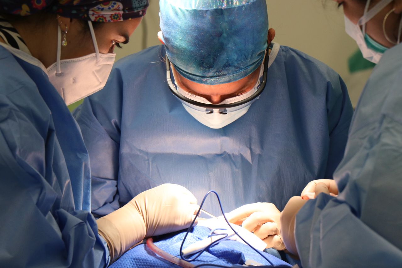 Surgeons in operation room wearing masks and gloves performing surgery.